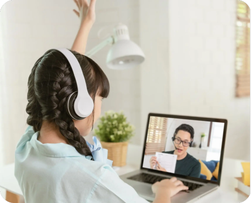 A girl with headphones raises her hand while engaged with her laptop, showcasing a moment of interaction or focus.