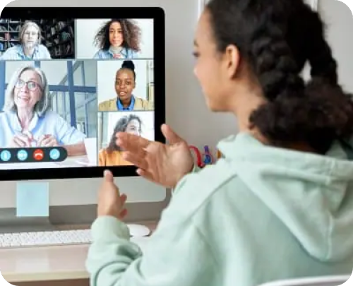 A woman engaged in a video chat on her computer, interacting with multiple participants on the screen.