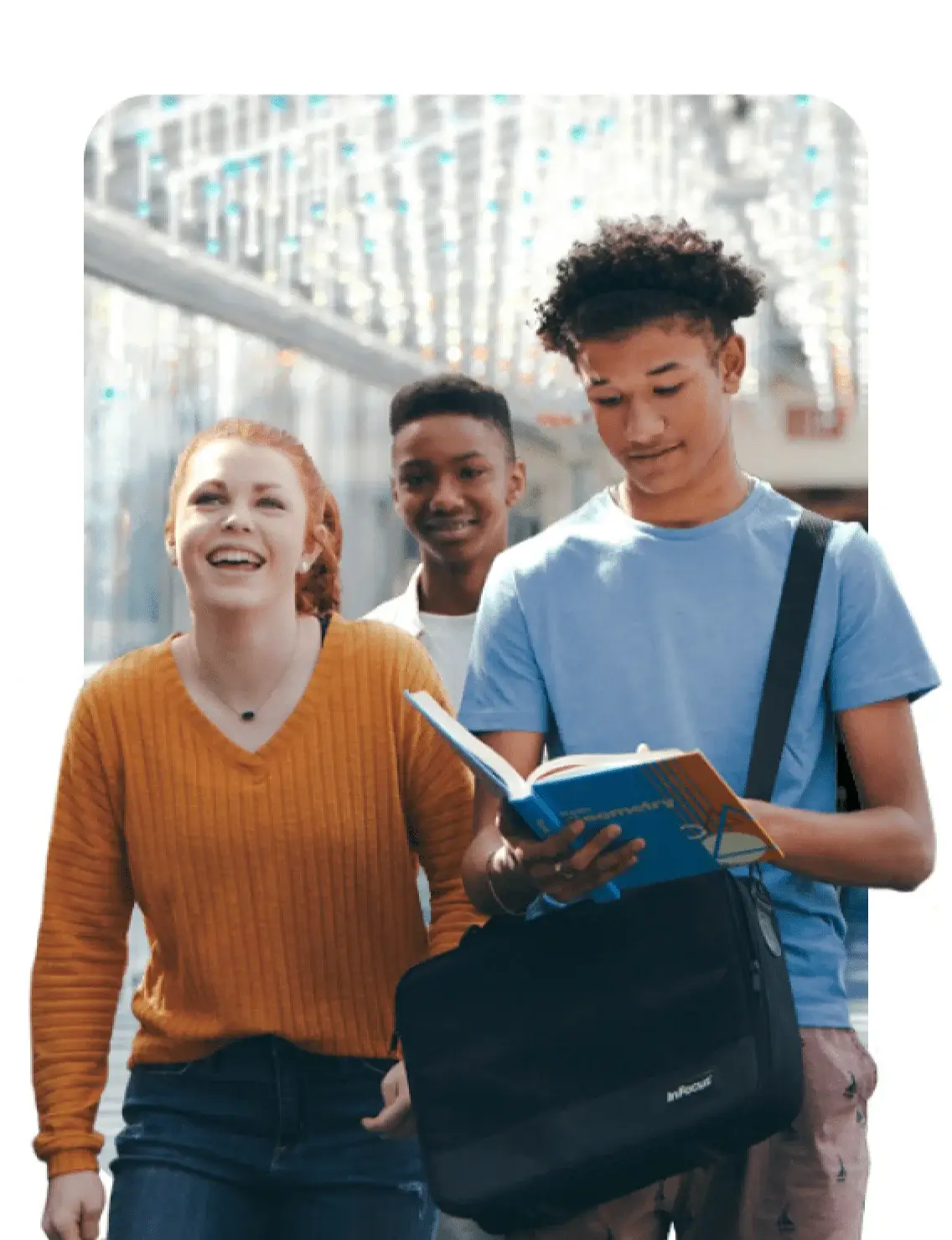 Three students walk down a hallway, each carrying a book, engaged in conversation and sharing ideas.