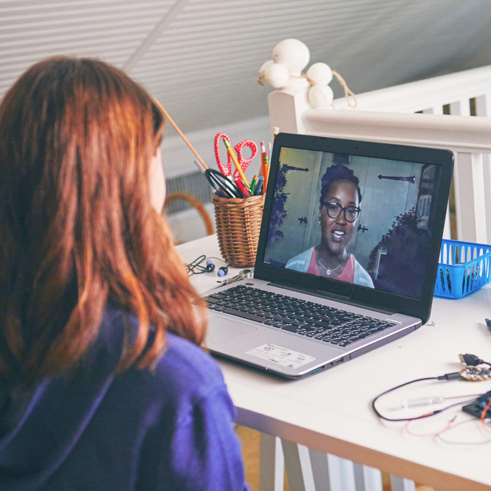 A woman seated at a desk, focused on her laptop, surrounded by a tidy workspace.