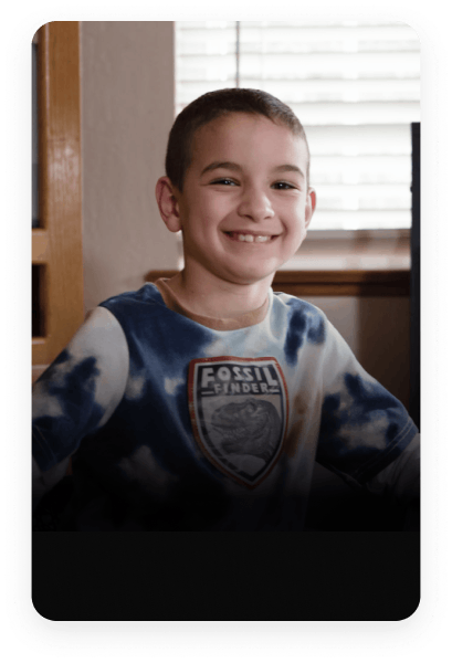 A young boy smiles joyfully while standing in front of a television screen