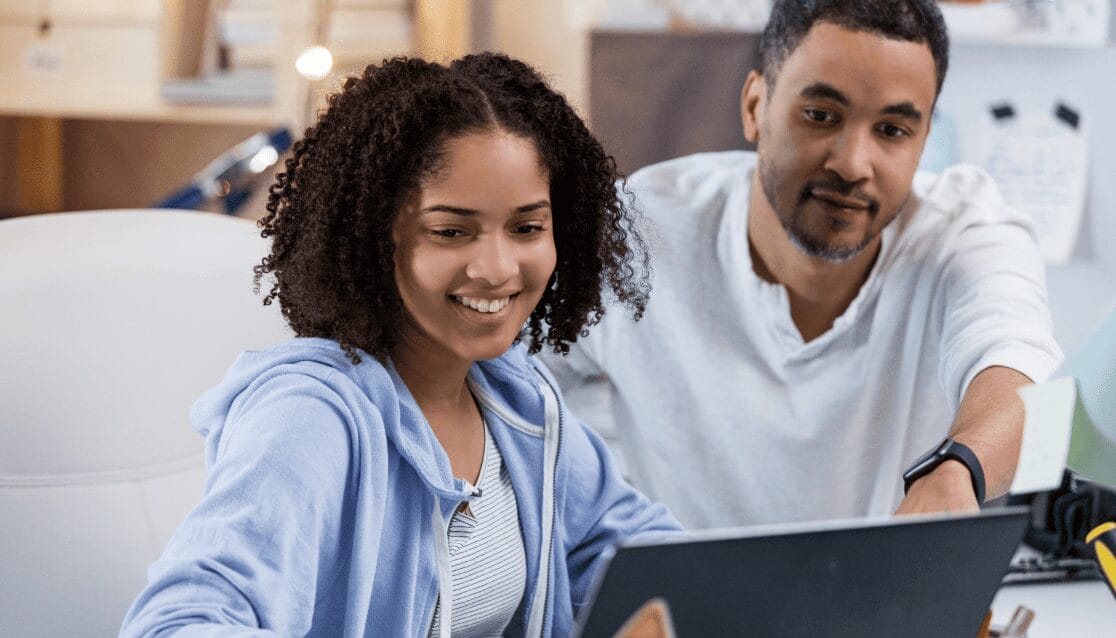 A man and woman smile together as they collaborate on a laptop, showcasing teamwork and positivity in their work environment.