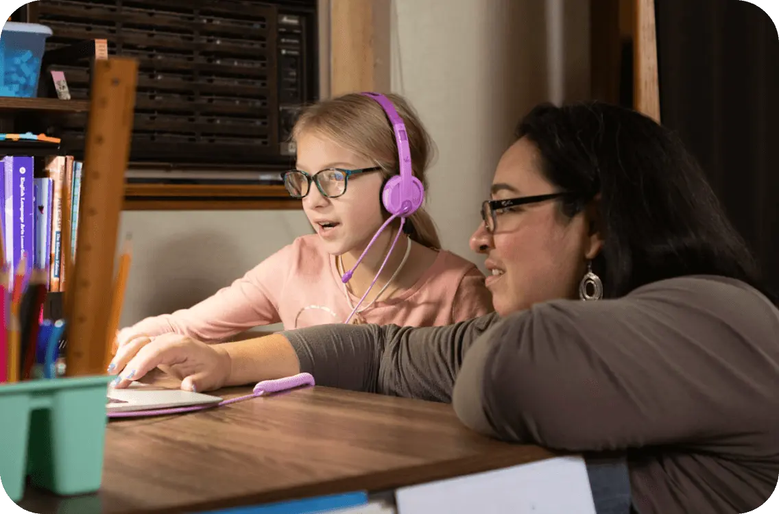  A woman and a girl wearing headphones, focused on their work at a computer, engaged in a collaborative task.