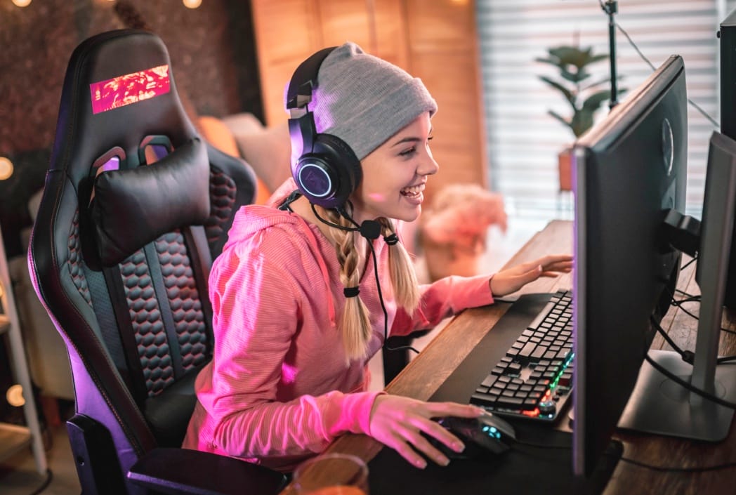Una mujer con un sombrero rosa y auriculares se dedica a jugar un videojuego, destacando su concentración y disfrute.