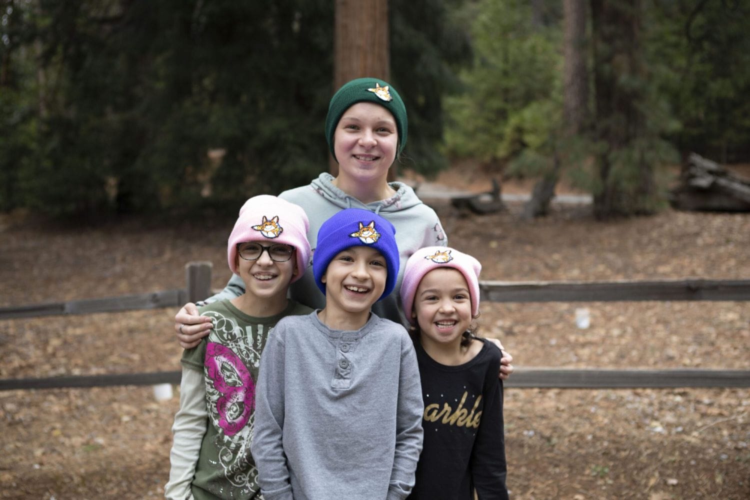 Un grupo sonriente de cuatro niños con gorros de colores con parches de animales. Están parados en un bosque, irradiando calidez y alegría.