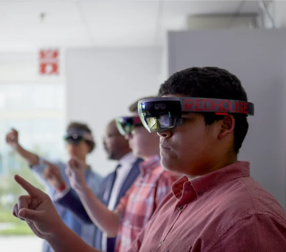 Un grupo de cuatro personas usa auriculares de realidad aumentada, de pie en una habitación con expresiones enfocadas, apuntando hacia adelante. Transmiten una sensación de compromiso futurista.