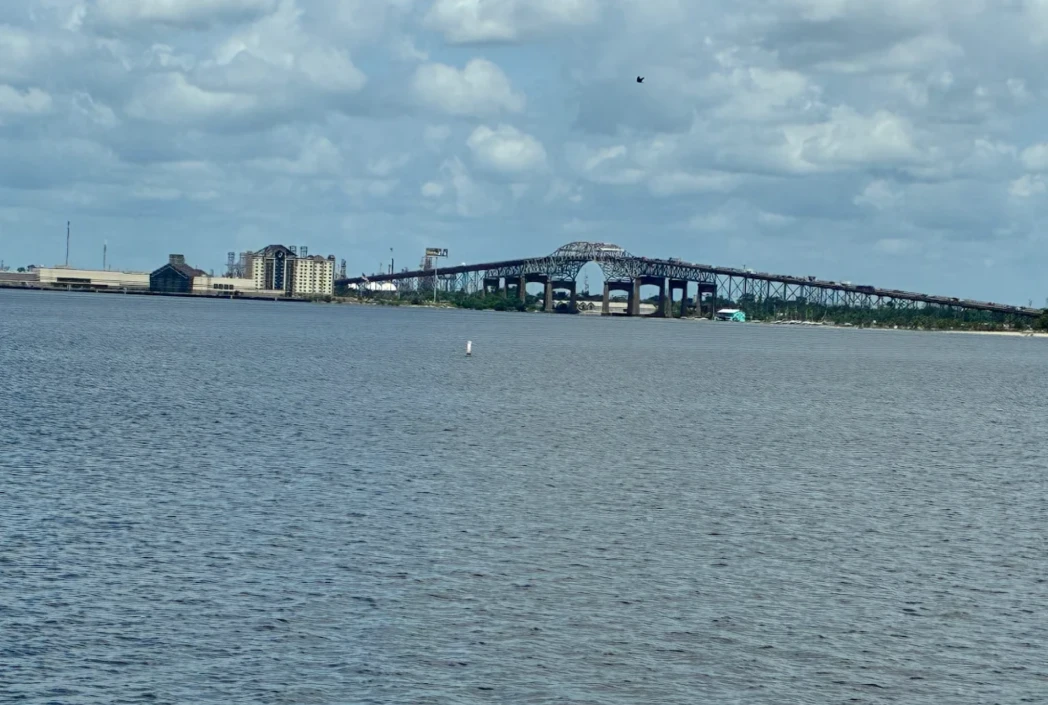 A wide river with a distant bridge and cityscape under a partly cloudy sky. The bridge spans across the water, evoking a serene and expansive atmosphere.