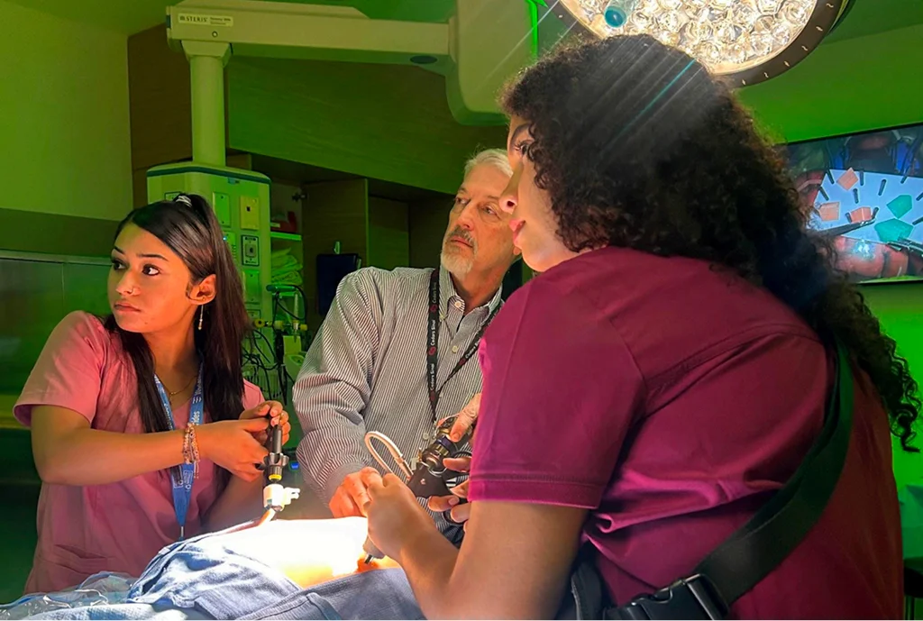 Un grupo de tres profesionales médicos en una sala de operaciones bien iluminada, se centró en un procedimiento. La escena transmite trabajo en equipo y concentración.