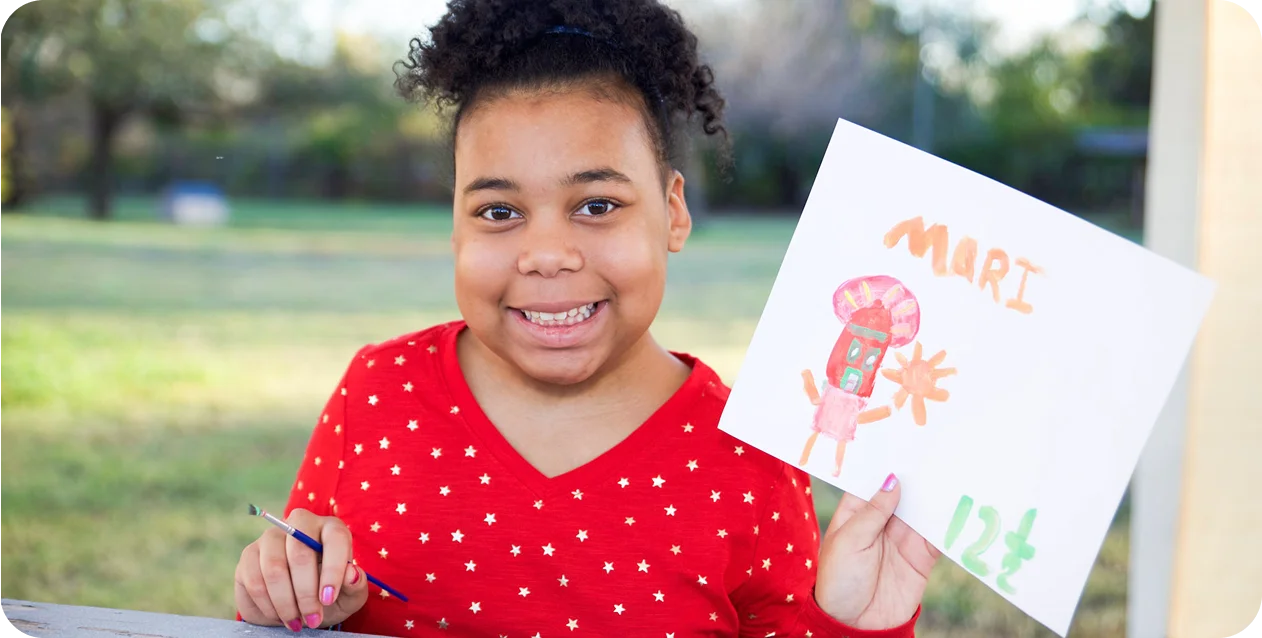 A smiling child in a red polka dot shirt holds up a colorful drawing outdoors. The art includes vibrant shapes and the text "MARI" and "12" in bold letters.