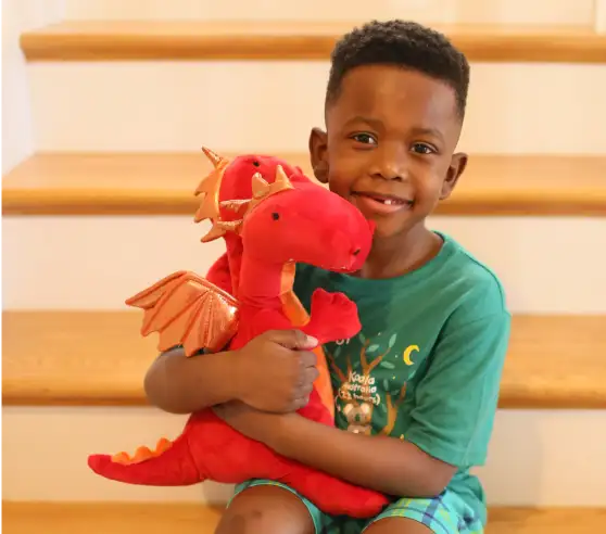 Una mujer y un niño se sientan en una mesa, sonriendo el uno al otro mientras sostienen el papel. Coloridos dibujos de niños se muestran en la pared detrás de ellos.