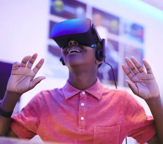 A person wearing a VR headset smiles with excitement, hands raised. They're in a room with blurred screens, creating a futuristic, immersive atmosphere.